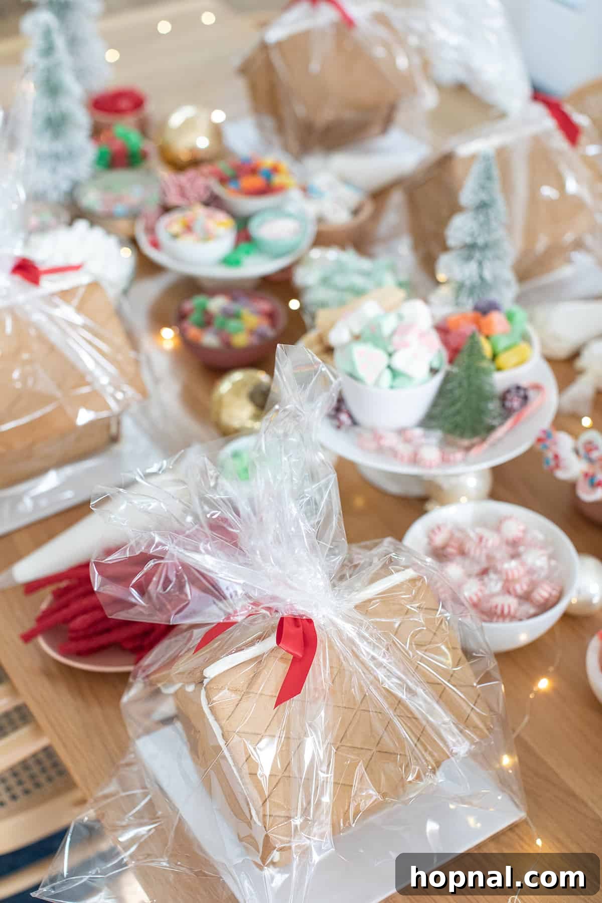 A festive gingerbread house party setup with kits, candies, and piping bags on a decorated table.