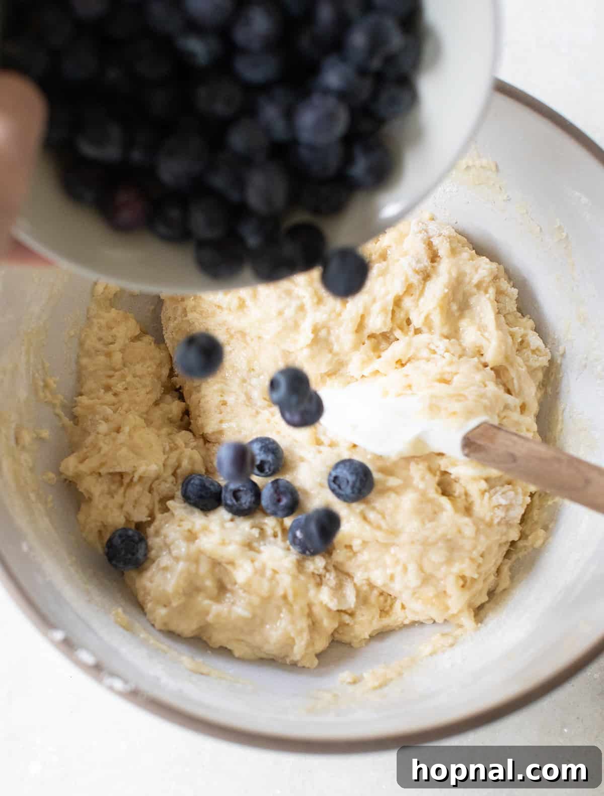 Golden Banana Blueberry Treats 5 Fresh blueberries being gently folded into a rich banana muffin batter, ready for baking.