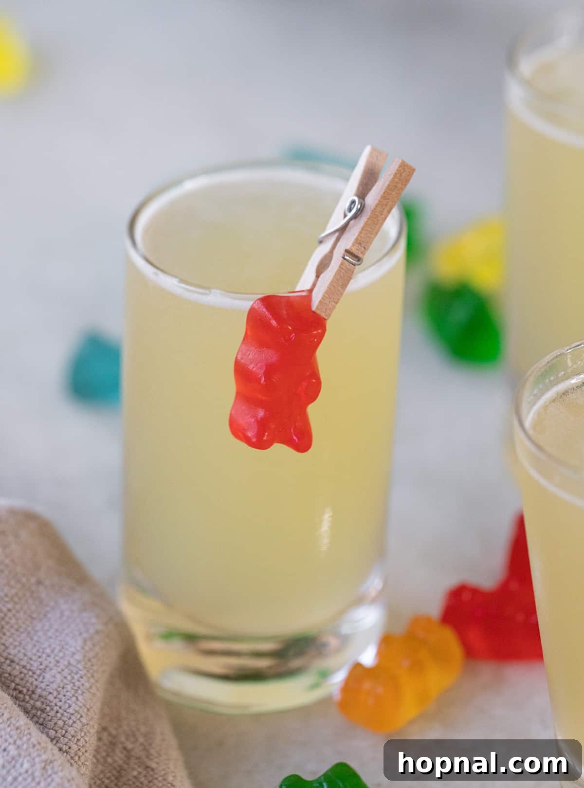 Tipsy Teddy Shot 2 A single Gummy Bear Shot in a clear glass, beautifully garnished with a white gummy bear clipped to the rim, sitting on a light background.