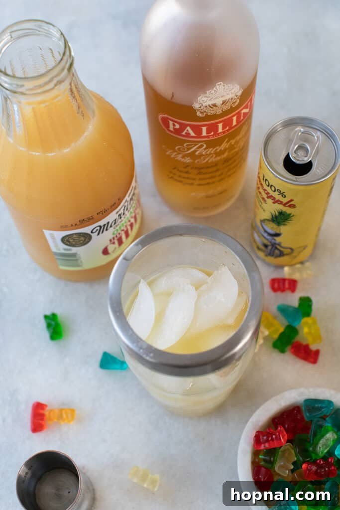 Tipsy Teddy Shot 4 All ingredients for Gummy Bear Shots laid out on a marble counter, including bottles of raspberry vodka, peach schnapps, and various juices.