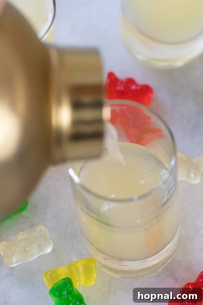 Tipsy Teddy Shot 6 A Gummy Bear Shot mixture being poured from a cocktail shaker into a small shot glass.
