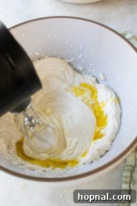 Adding olive oil into the whipped cheese mixture slowly.