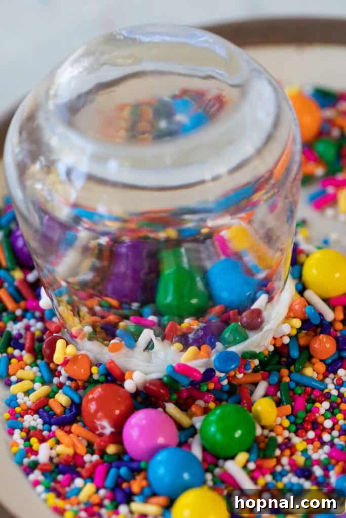A shot glass being dipped into a bowl of colorful sprinkles to create a festive rim.