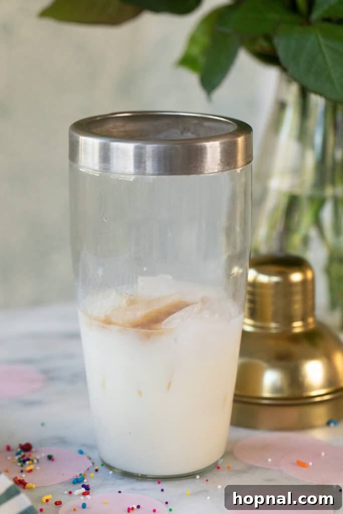 A cocktail shaker filled with ice and the liquid ingredients: vodka, white chocolate liqueur, and vanilla extract.