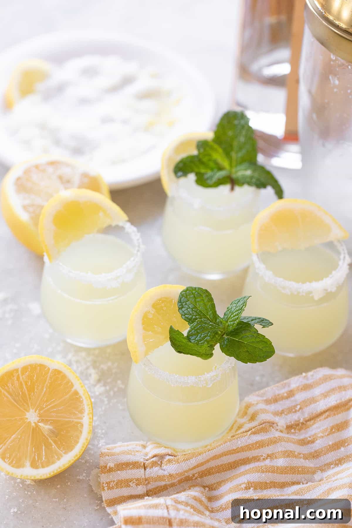 Lemon drop shots in sugar-rimmed glasses with lemon wedges and fresh mint garnish, ready for a party.