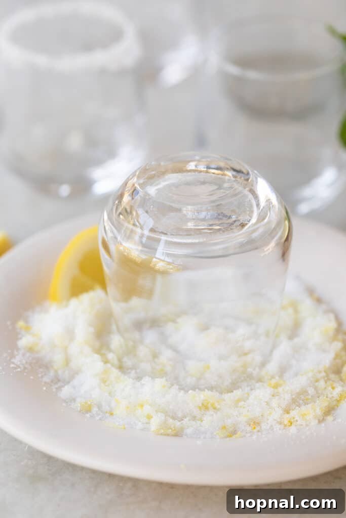 A shot glass being inverted and dipped expertly into a plate of granulated sugar to coat its rim evenly.