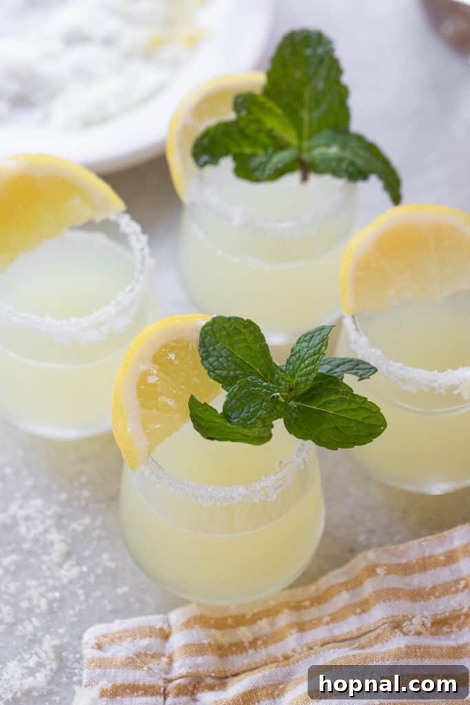 A beautifully garnished lemon drop shot with fresh mint leaves and a lemon wedge, gleaming with a sugared rim, ready to be enjoyed.
