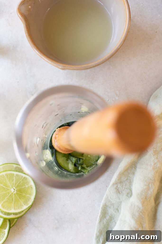 Muddling fresh cucumber slices and lime juice in a cocktail shaker, releasing their vibrant flavors.