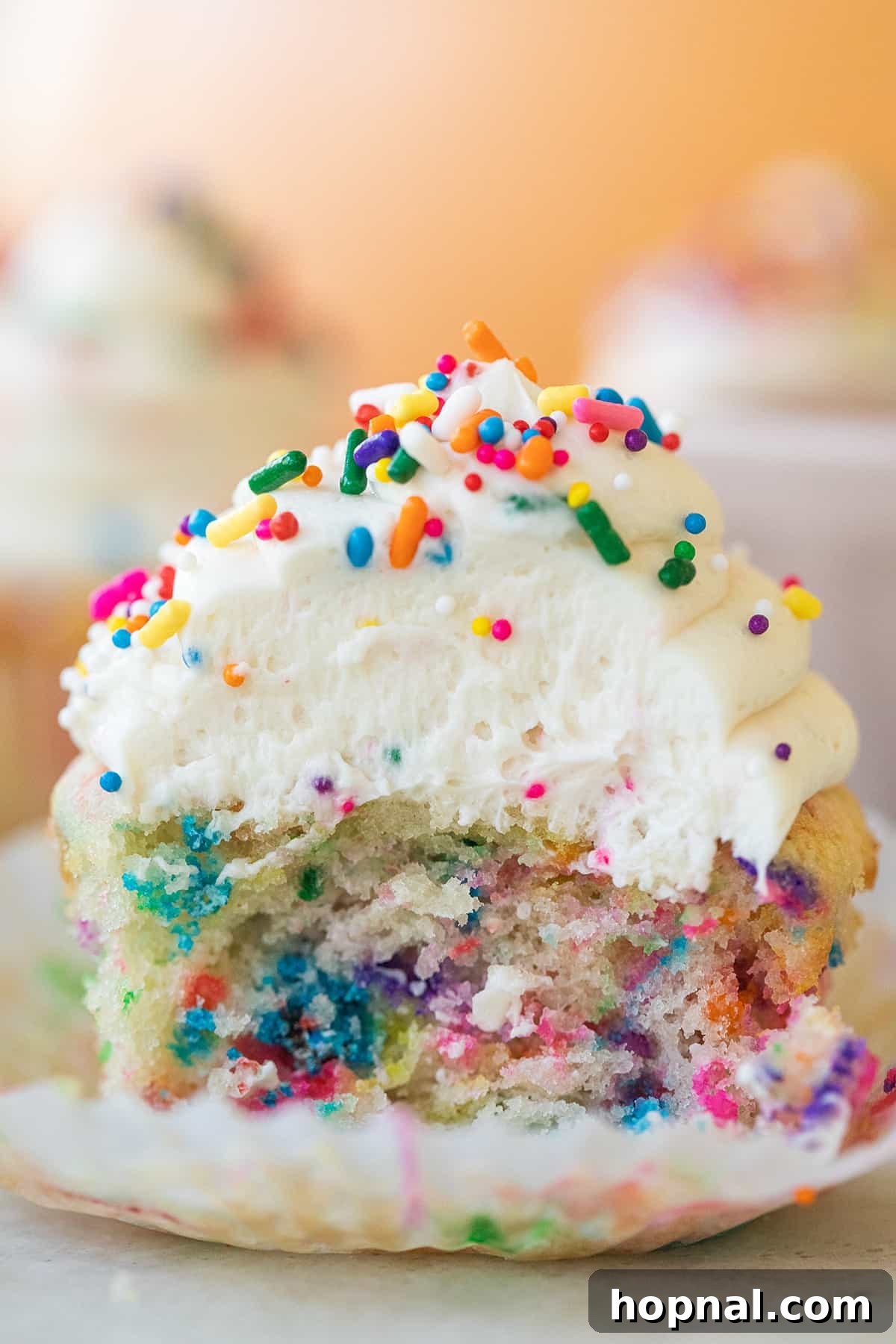 Moist funfetti cupcake with colorful sprinkles and a bite taken out to show the soft crumb. 