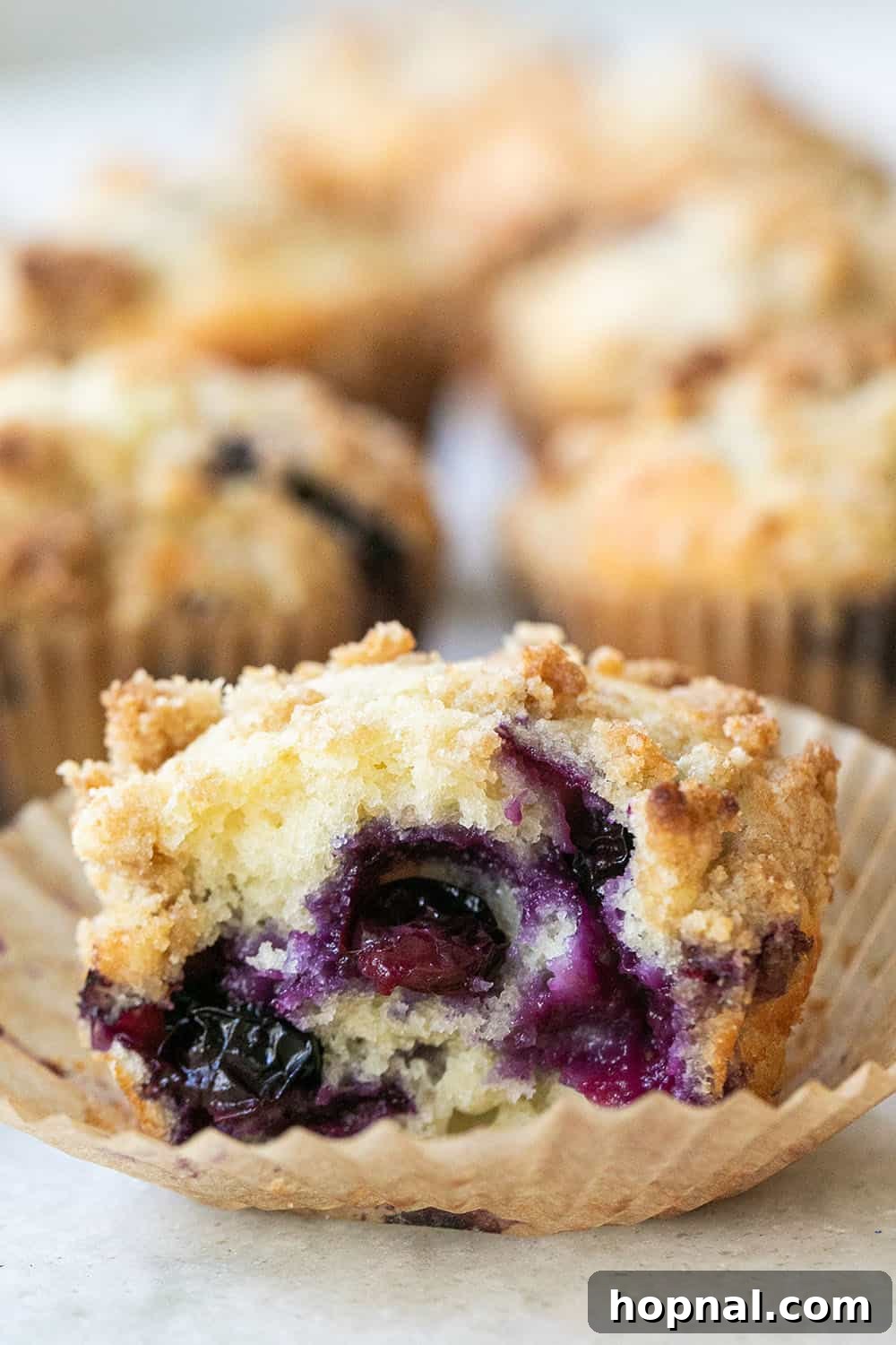 A close-up of easy blueberry muffins, showing juicy blueberries embedded in a tender, buttery crumb, achieved by using a thoughtful combination of butter and oil for ultimate moisture.