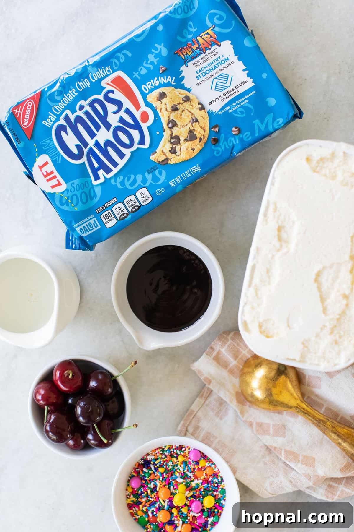 An array of delicious milkshake toppings spread out, including a scoop of rich vanilla ice cream, decadent chocolate sauce, a handful of classic Chips Ahoy cookies, colorful sprinkles, and vibrant cherries. These are all the ingredients needed to create a visually appealing and tasty cookie milkshake.