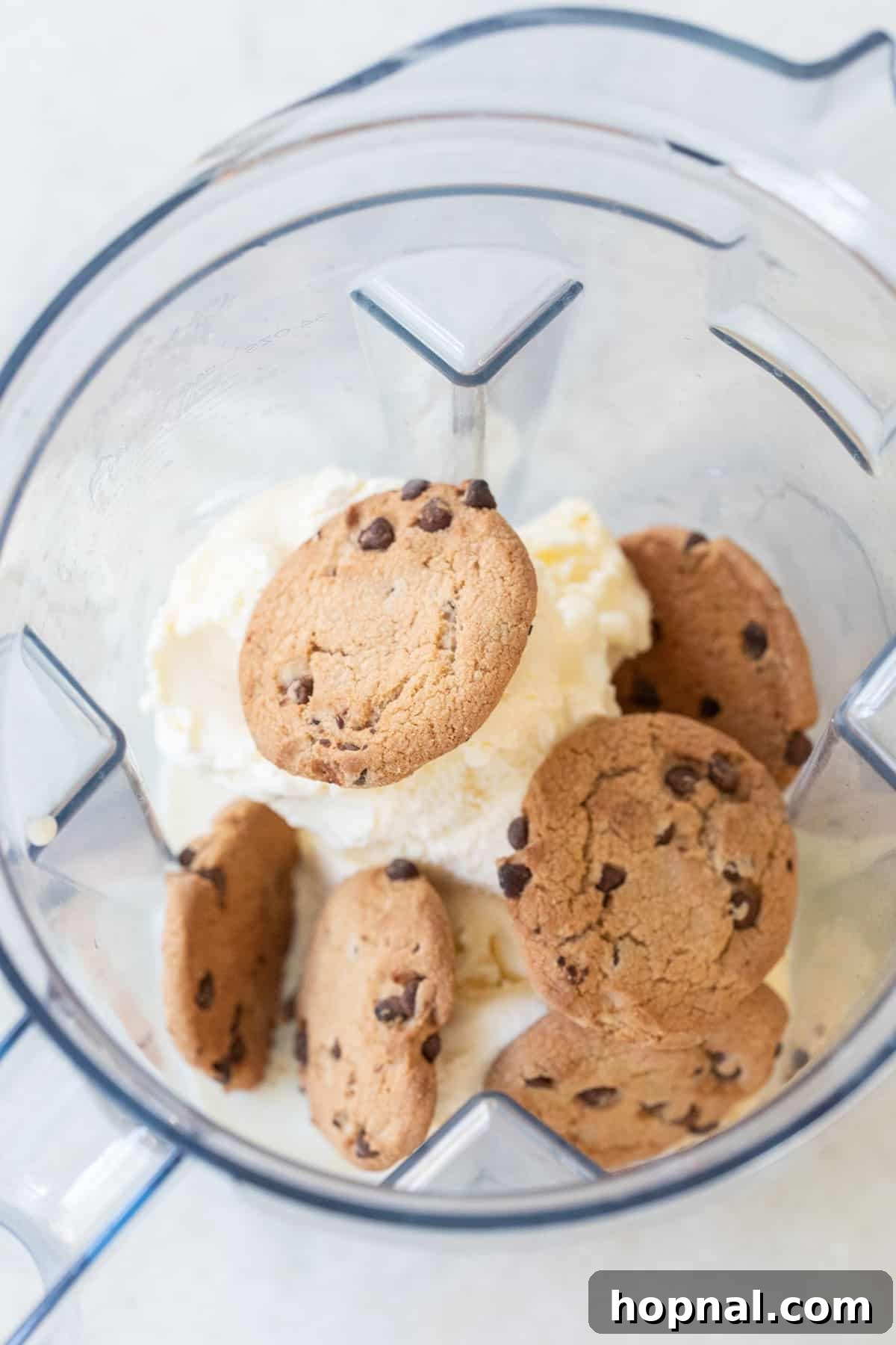 Three whole Chips Ahoy chocolate chip cookies being added to a blender, ready to be transformed into a creamy milkshake. Alongside, a scoop of vanilla ice cream and a splash of milk are implied, highlighting the simple ingredients needed for this easy dessert recipe.