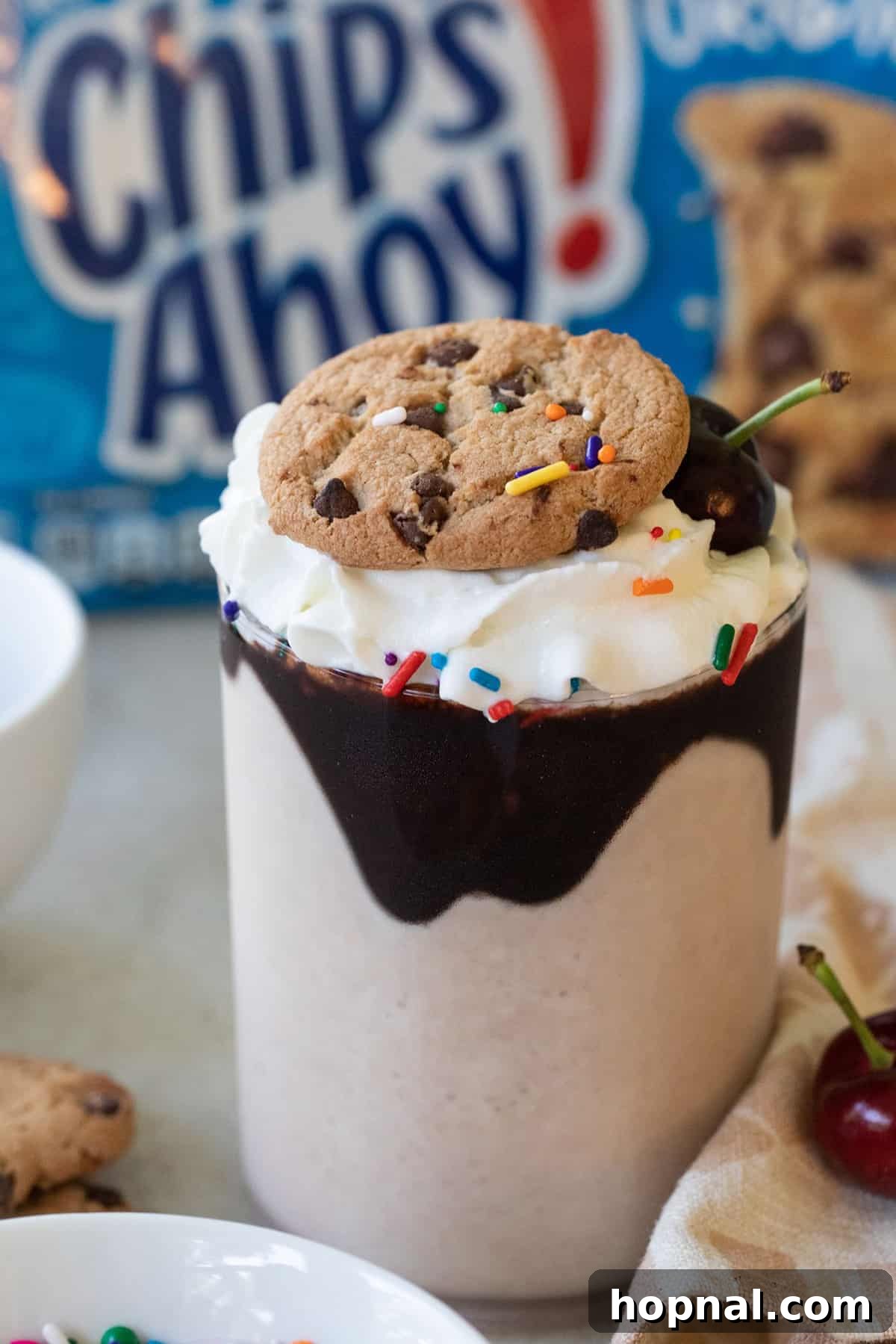 A perfectly blended chocolate chip cookie milkshake served in a tall glass, generously topped with whipped cream and garnished with a whole Chips Ahoy cookie, ready to be enjoyed as a refreshing and indulgent treat.