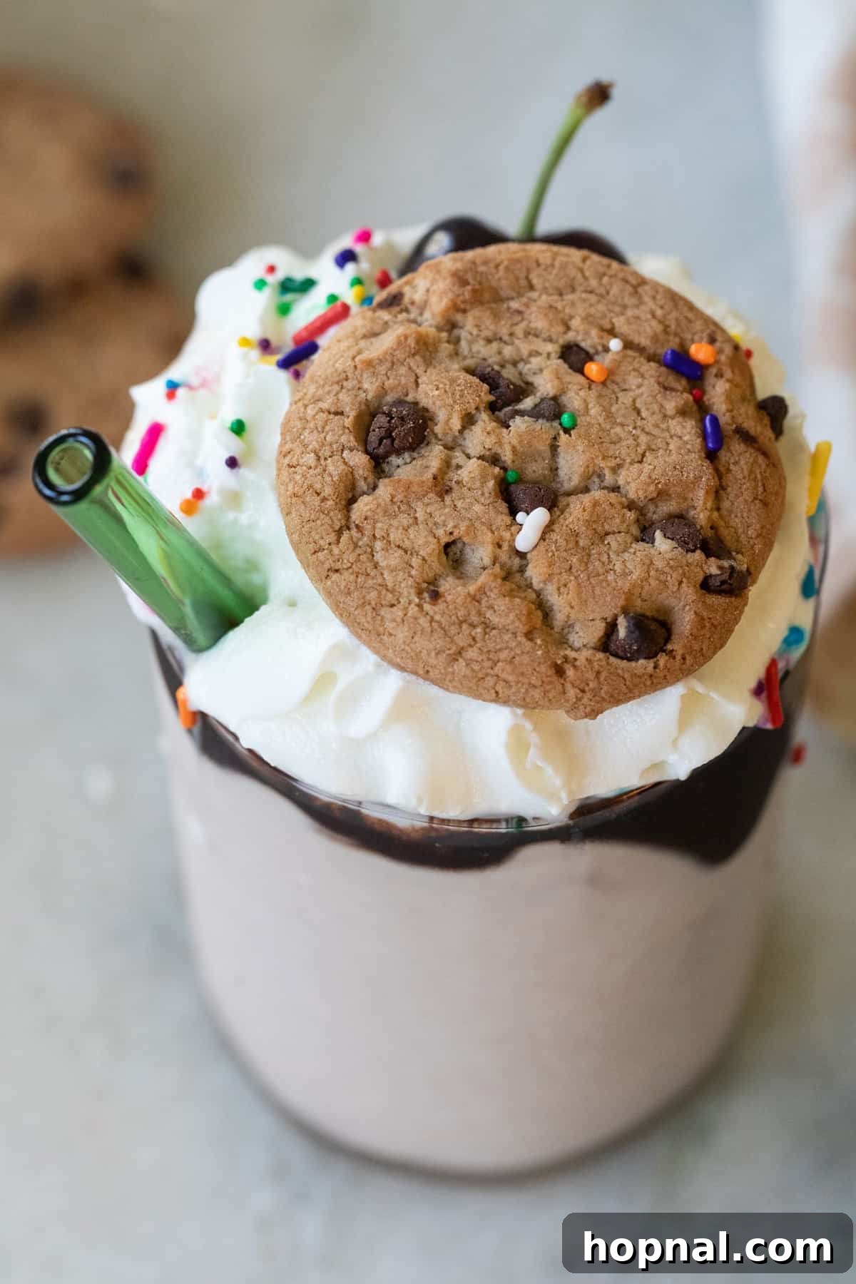 A close-up of a delightful chocolate chip cookie milkshake, artfully garnished with a whole Chips Ahoy cookie sitting perfectly on a cloud of whipped cream, inviting you to take a delicious sip.