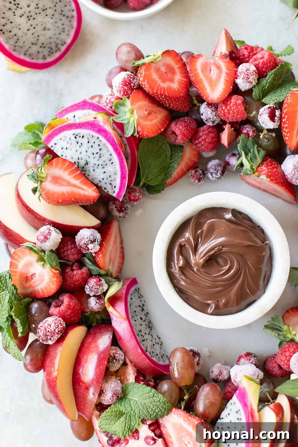 Christmas Wreath Fruit Platter with Dip A beautifully arranged Christmas fruit platter in the shape of a wreath, accompanied by a side of rich chocolate dipping sauce, ready for serving.