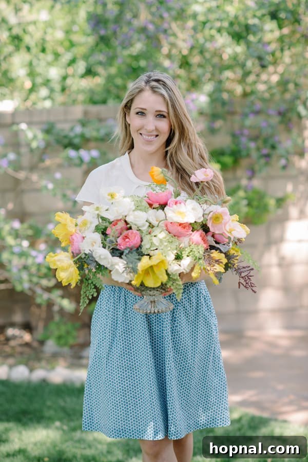 Mom's Garden Tea Oasis 10 Eden Passante, holding a large, vibrant floral bouquet in a lush backyard setting