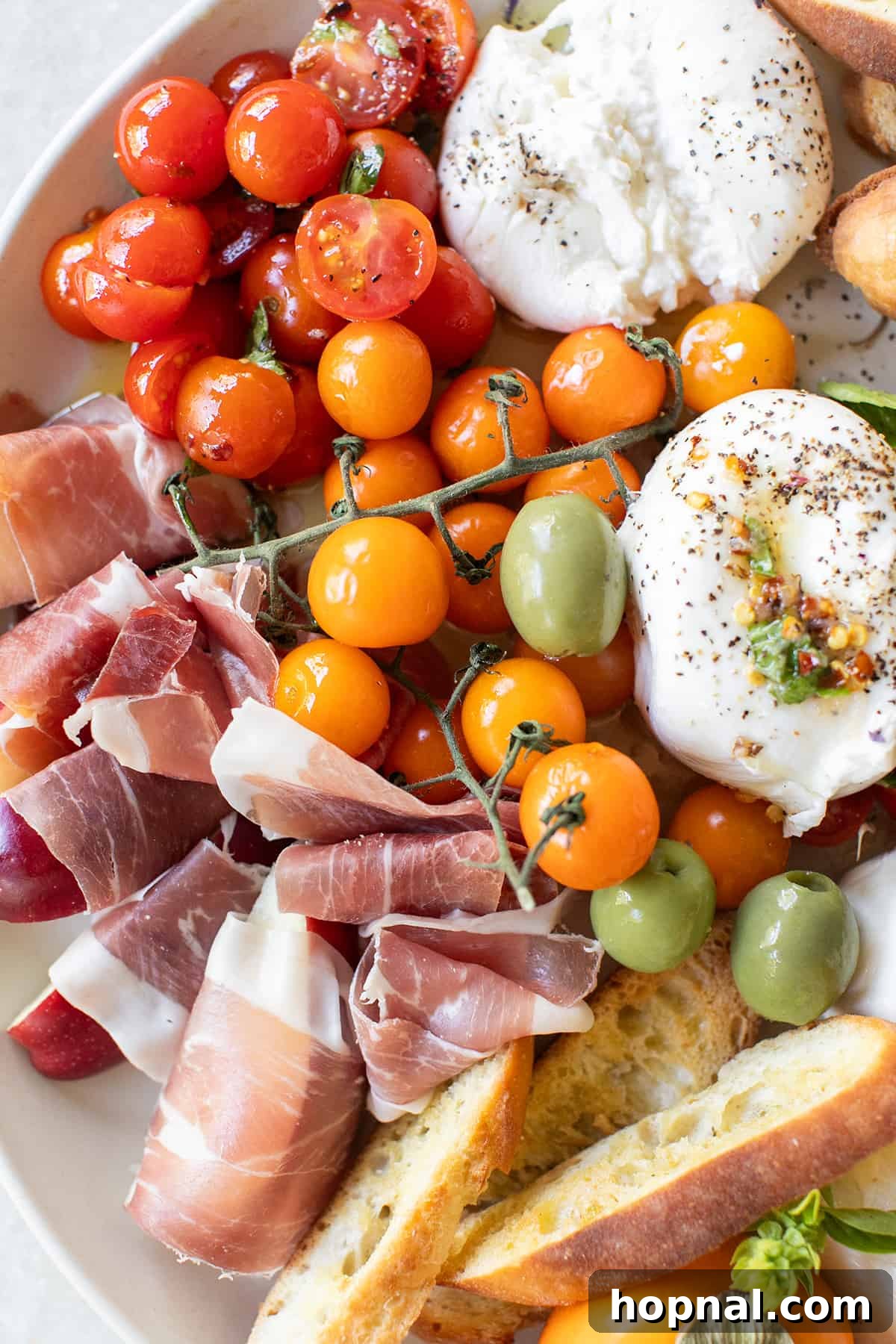 A simple yet elegant burrata platter featuring creamy burrata, crispy crostini, gourmet crackers, fresh fruit wrapped in savory prosciutto, and a variety of olives.