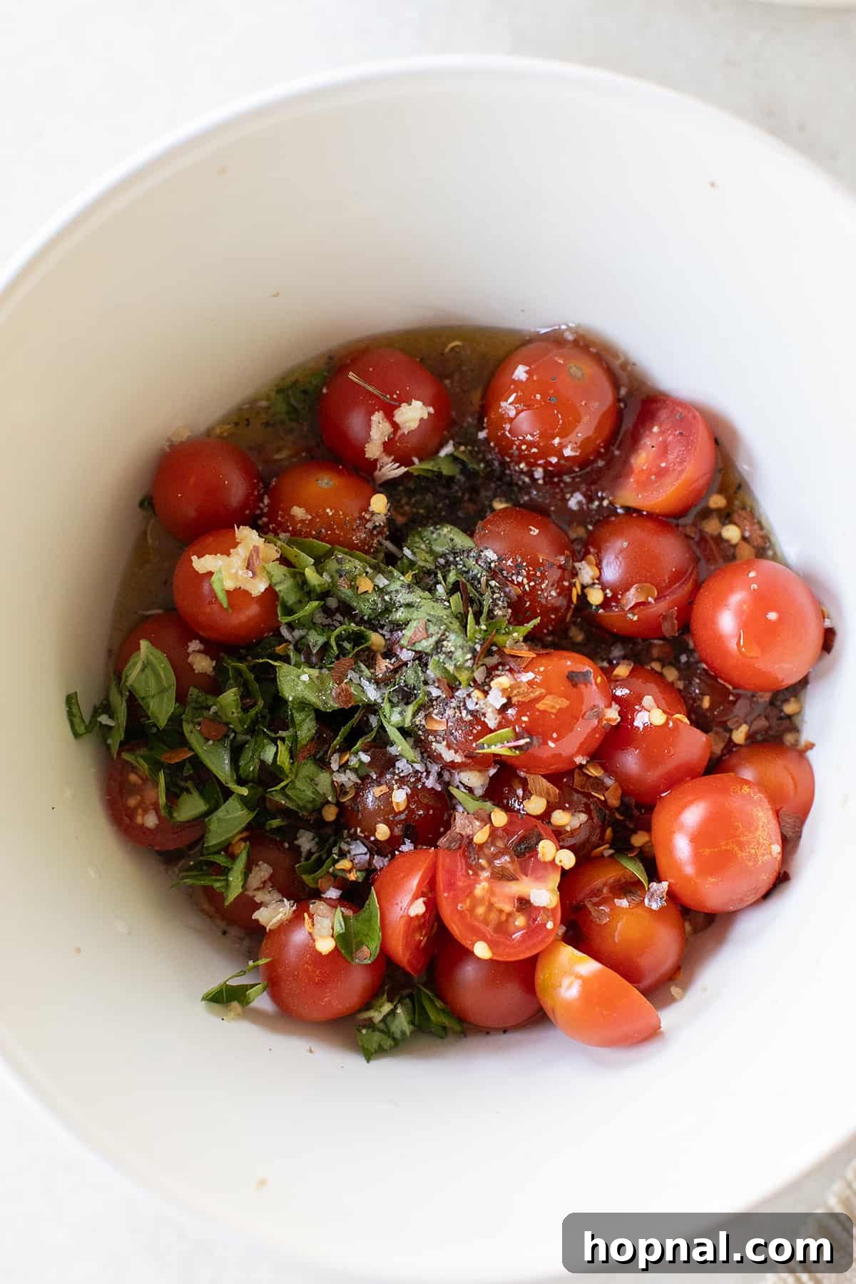 Close-up of a bowl brimming with marinated tomatoes infused with fragrant garlic, fresh thyme, a hint of chili flakes, and rich olive oil.