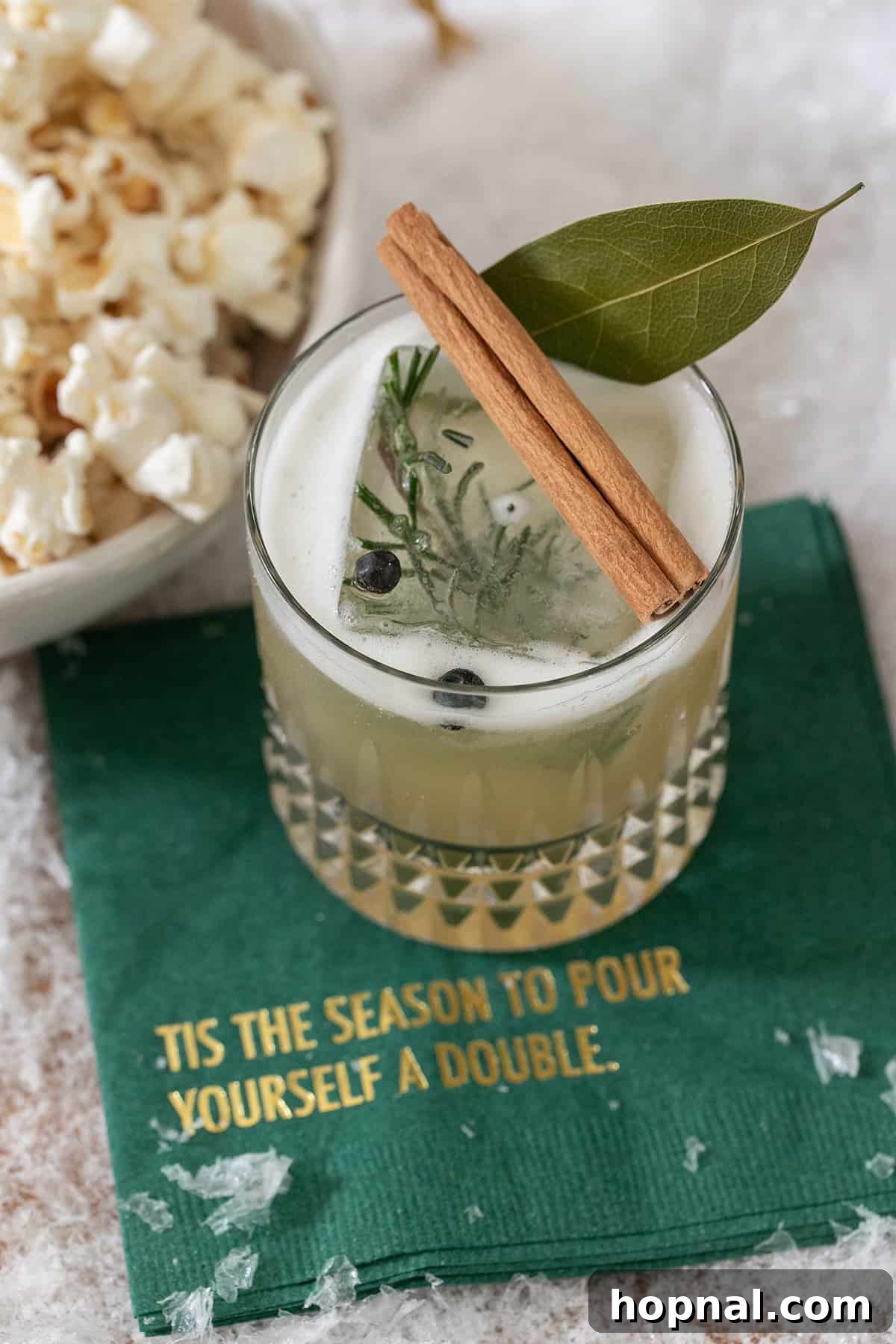 A beautifully garnished Wilderness Whiskey Sour cocktail with rosemary and spices in a glass.