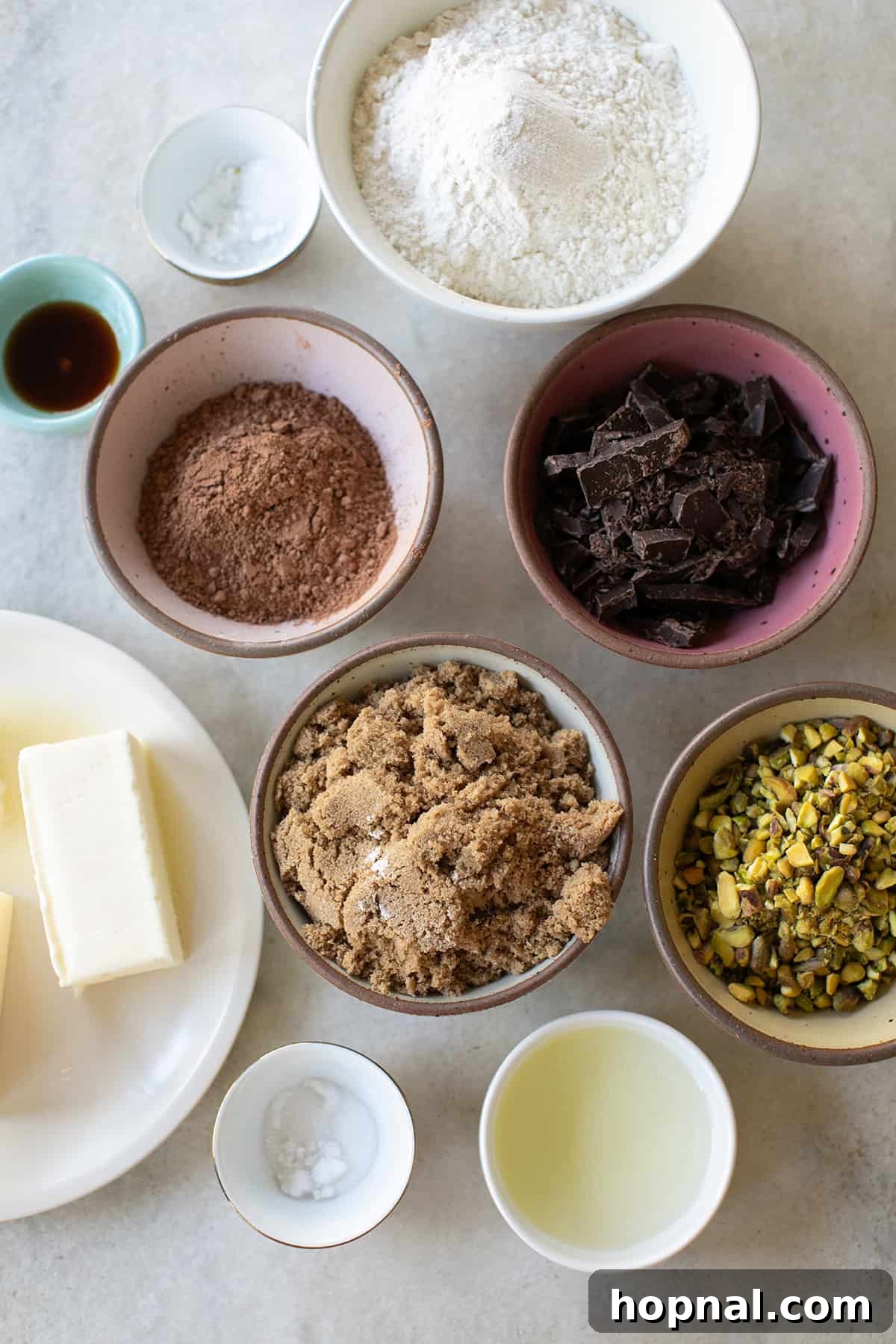 Individual bowls showcasing the essential ingredients for making delicious sable cookies: rich brown sugar, dark cocoa powder, all-purpose flour, creamy butter, a single egg, and vibrant pistachios.