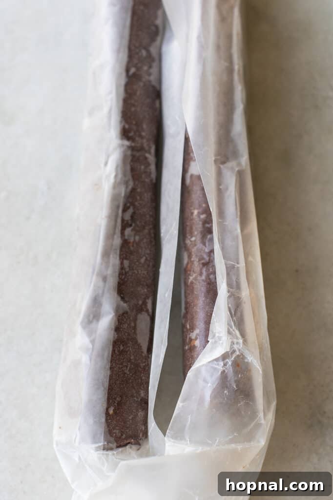 Chilled chocolate cookie dough, expertly wrapped in parchment paper and shaped into a log, ready for slicing and baking.