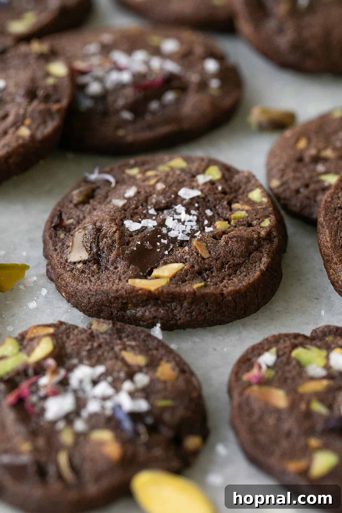 A close-up shot of perfectly baked chocolate sable cookies with vibrant green pistachios and glistening sea salt, ready to be enjoyed.