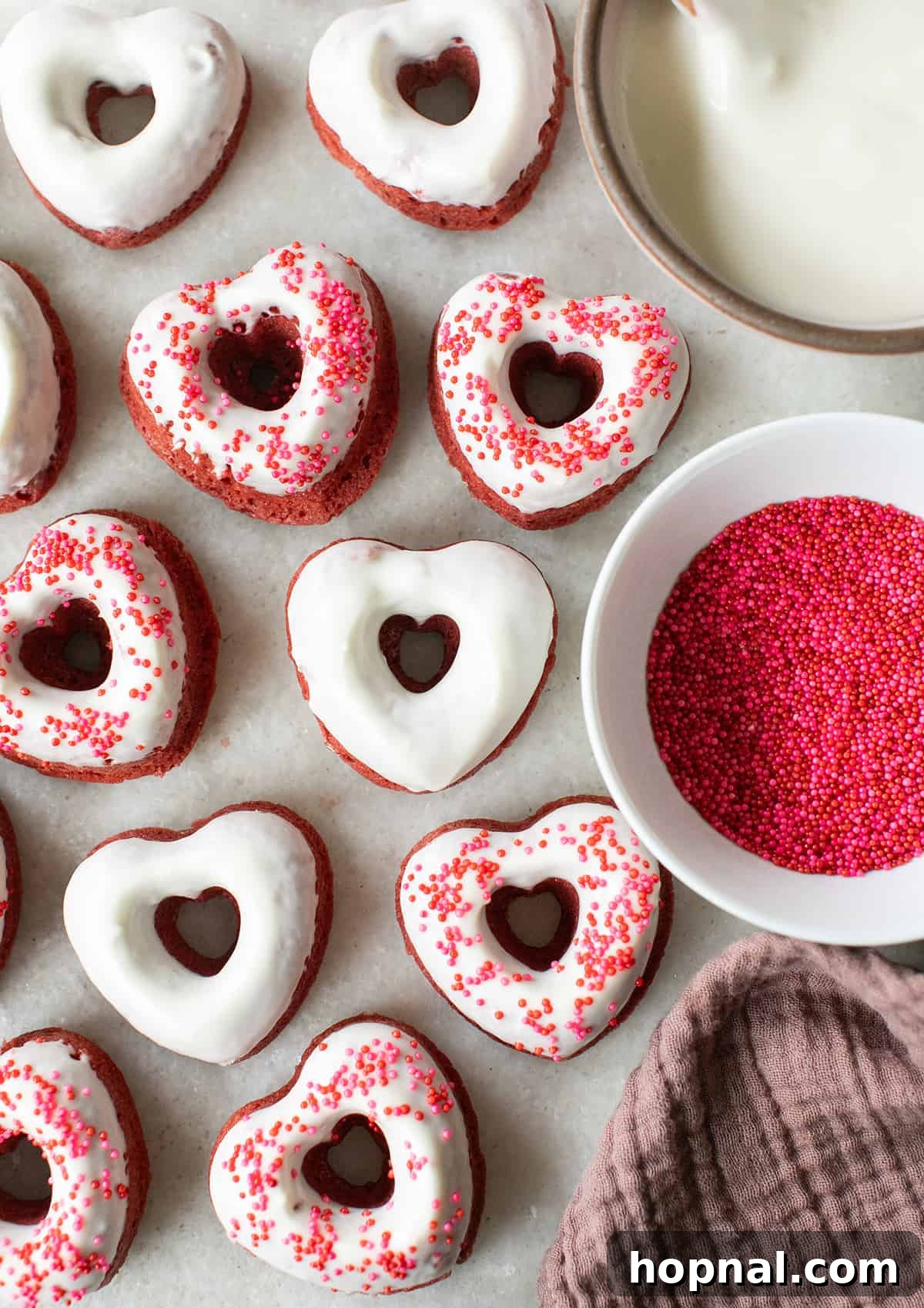 Freshly baked red velvet donuts, glistening with cream cheese glaze and topped with festive sprinkles, arranged beautifully for serving.