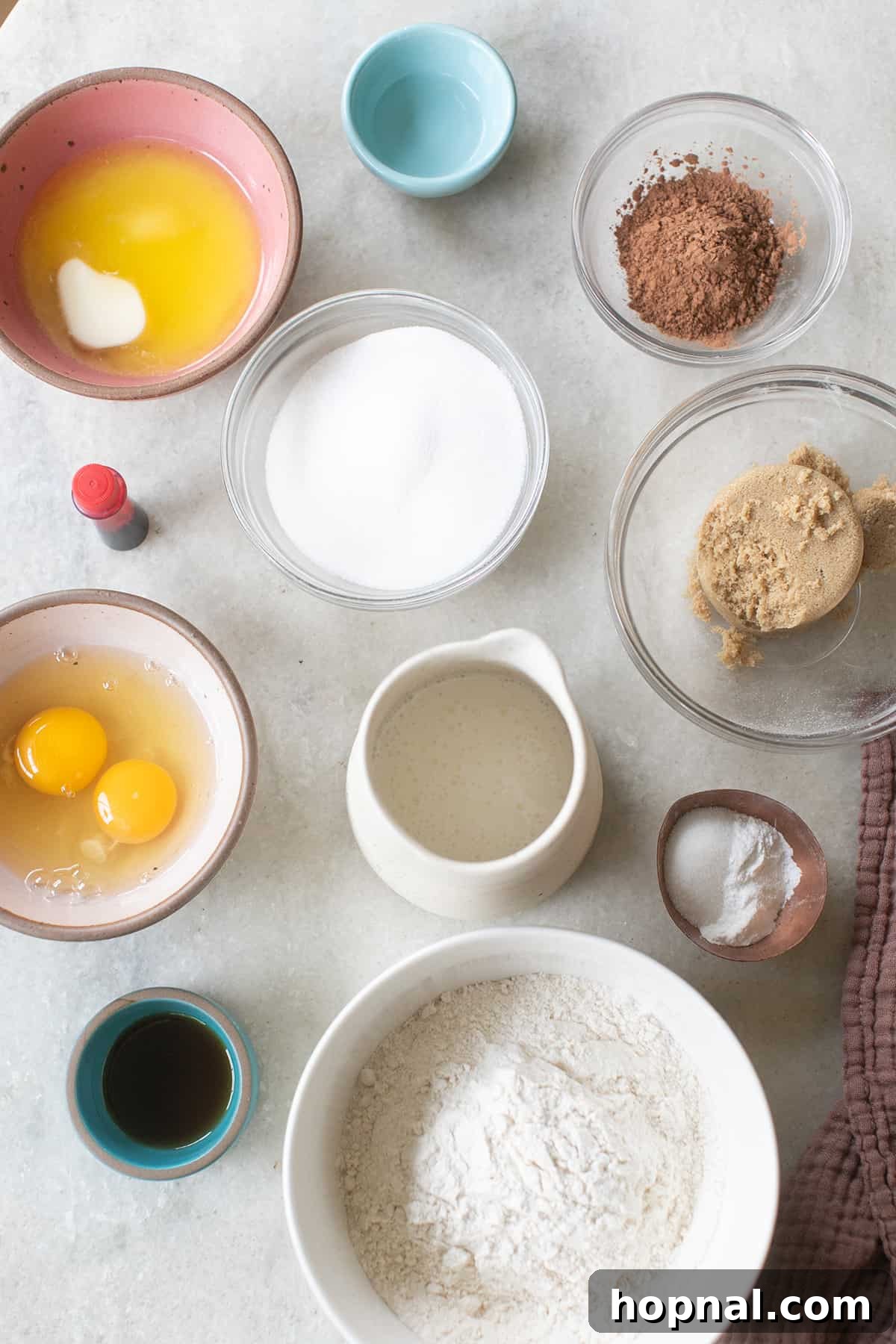 A selection of key ingredients for red velvet donuts, including eggs, buttermilk, vanilla extract, brown sugar, melted butter, flour, and a bottle of vibrant red food coloring, neatly arranged in small bowls.