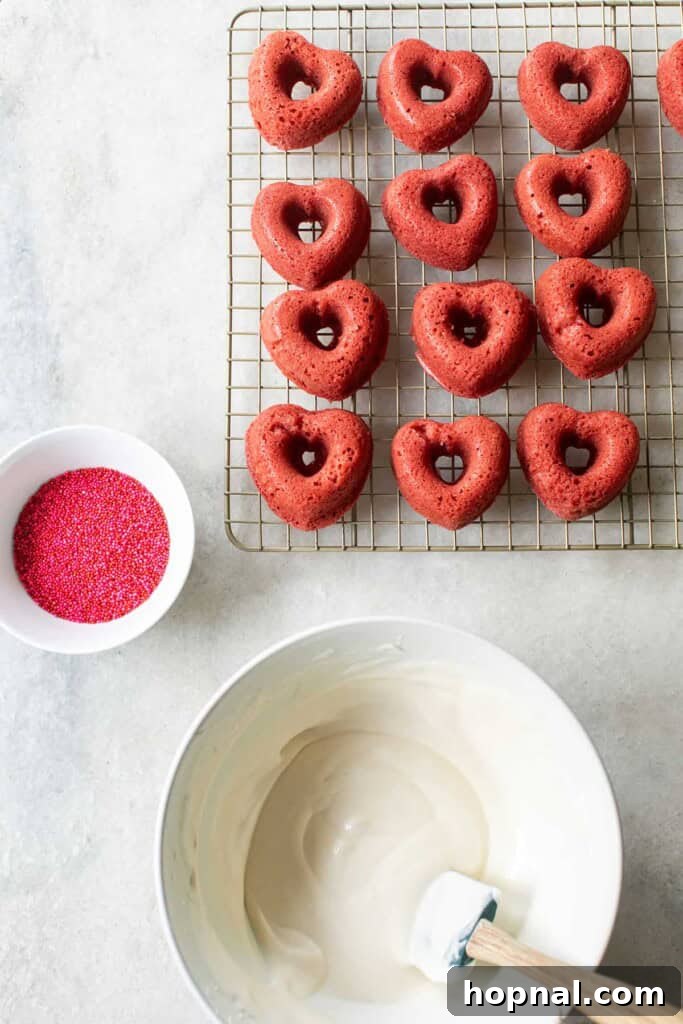 Platter of glazed red velvet donuts, some decorated with sprinkles, alongside a bowl of luscious cream cheese frosting.