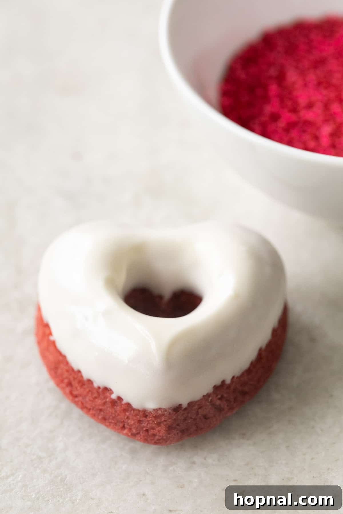A single, perfectly glazed red velvet cake donut, adorned with subtle sprinkles, inviting a delightful bite.