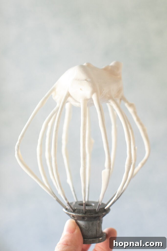 Maple syrup frosting clinging to a whisk attachment from a stand mixer, showing its thick and fluffy texture.