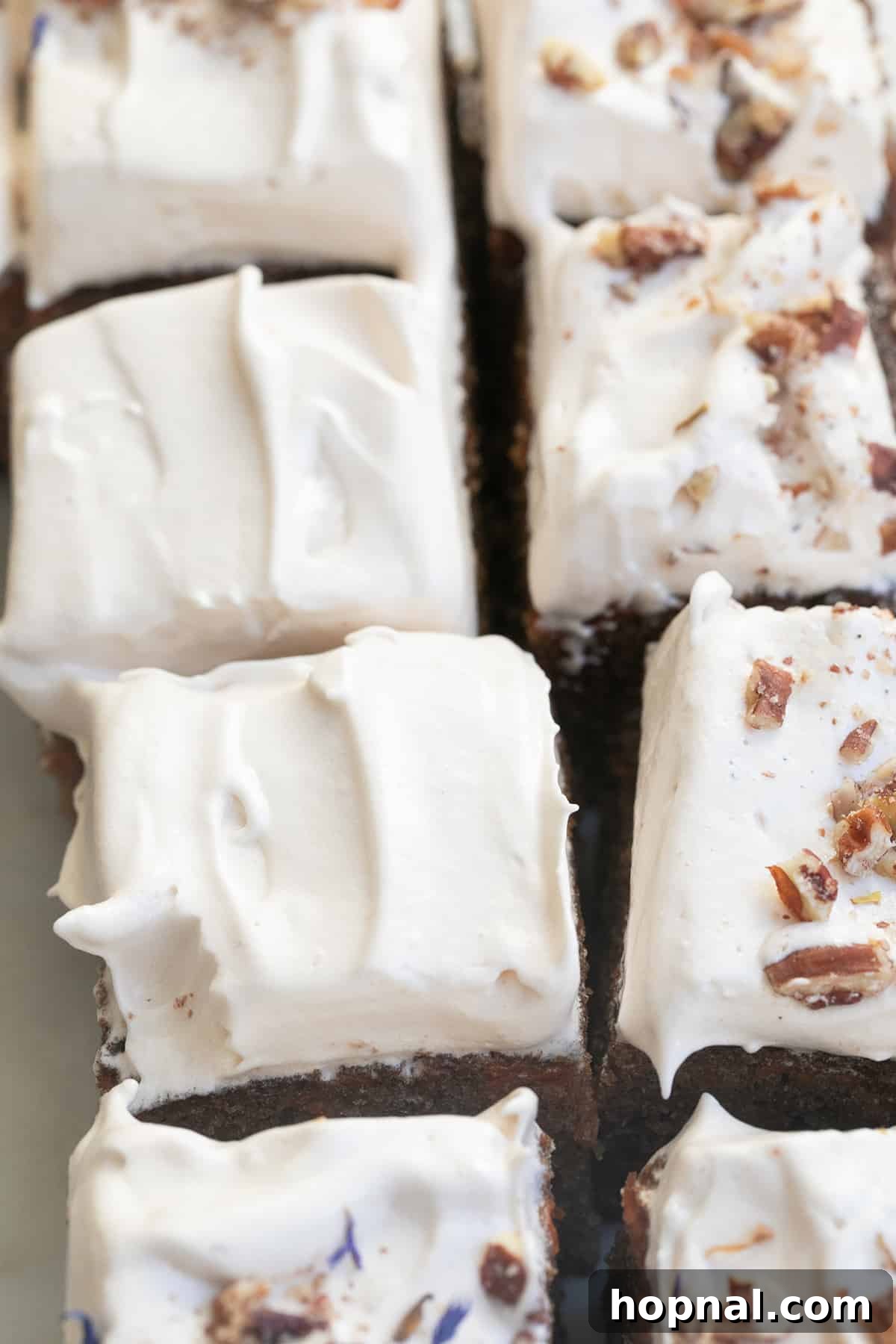 A slice of moist carrot cake generously topped with light maple syrup frosting and sprinkled with chopped pecans.