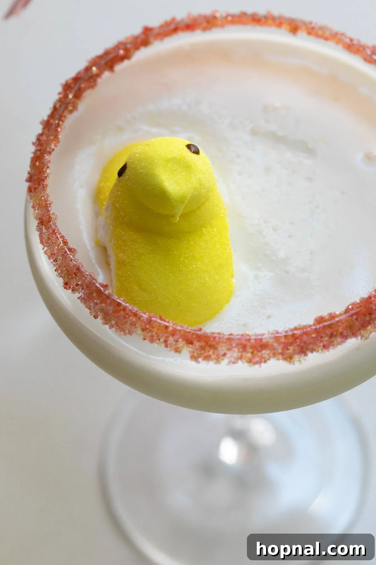 Peep martini, showcasing its creamy texture, adorned with a yellow Peep marshmallow and a bottle of marshmallow vodka in the background.