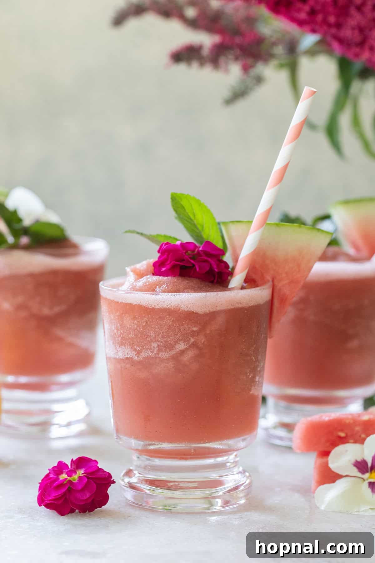 Easy watermelon frosé served in glasses with straws, garnished with flowers, on a tray for a summer party.