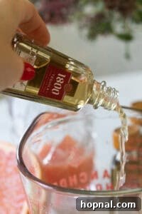 Pouring tequila shots into a glass jar for mixing.