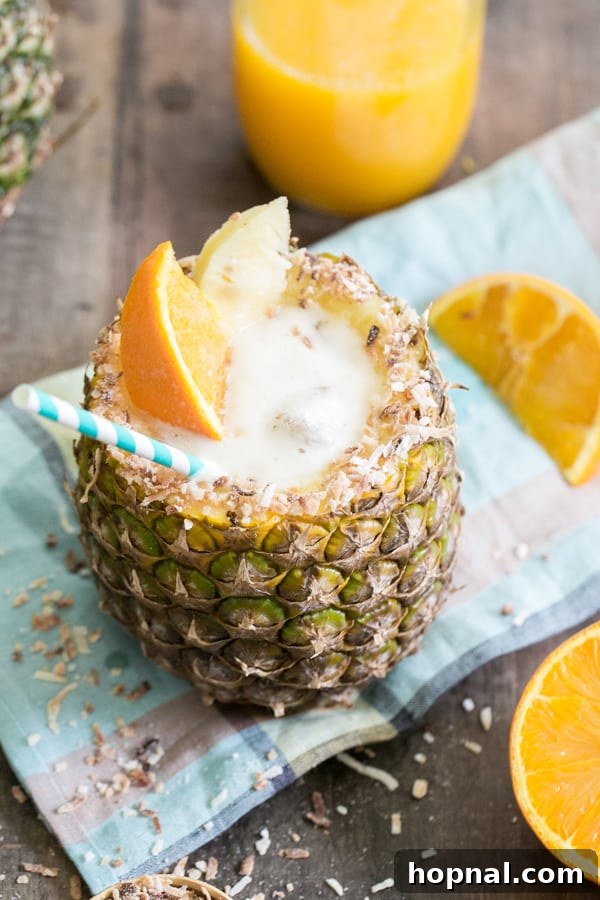 A vibrant pineapple rum cocktail served in a freshly carved pineapple cup, adorned with a blue straw and fresh orange slices, evoking a perfect tropical getaway.