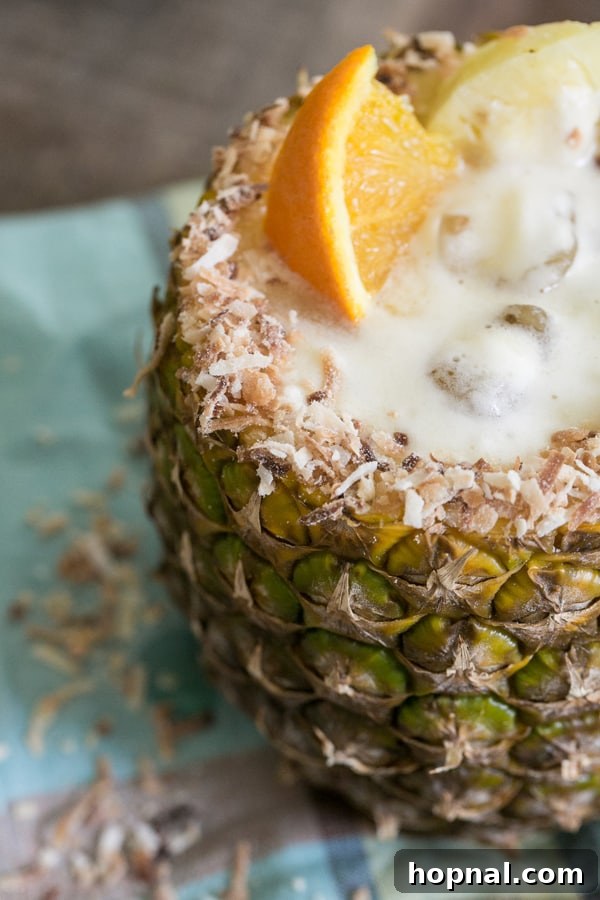 Close-up view of a pineapple rum cocktail served in a carved pineapple cup, with the rim beautifully garnished with golden toasted coconut flakes.