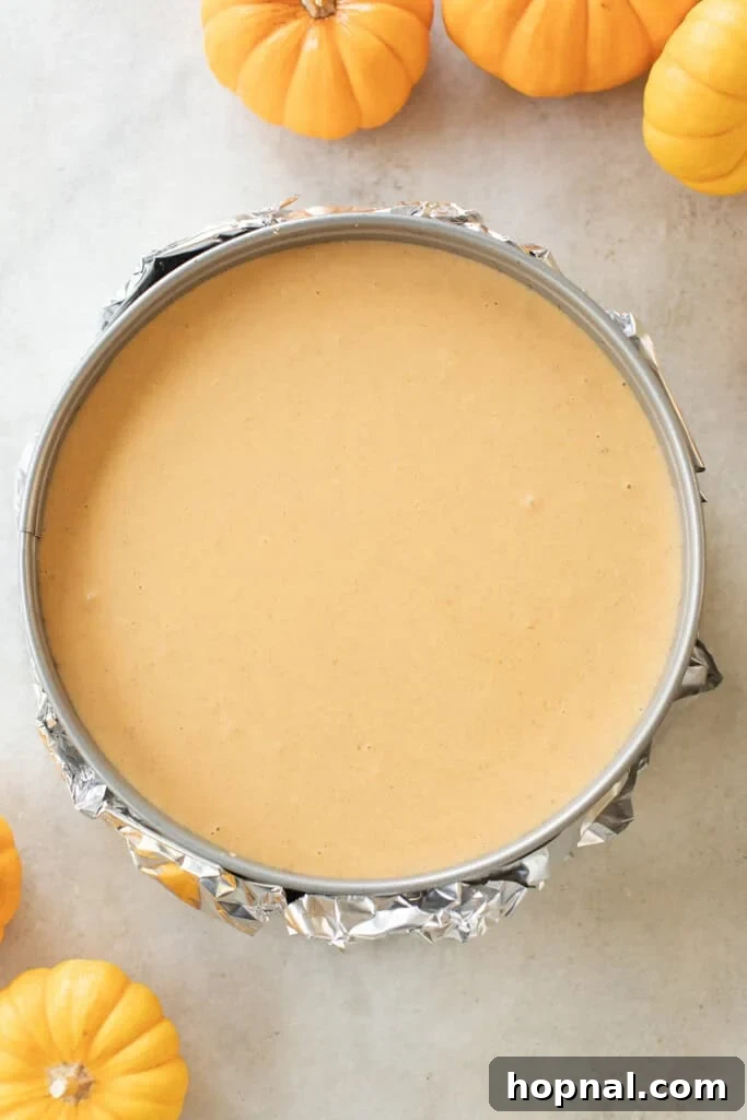 Pumpkin cheesecake in a foil-wrapped springform pan, filled and smoothed, before being placed into a water bath for baking.