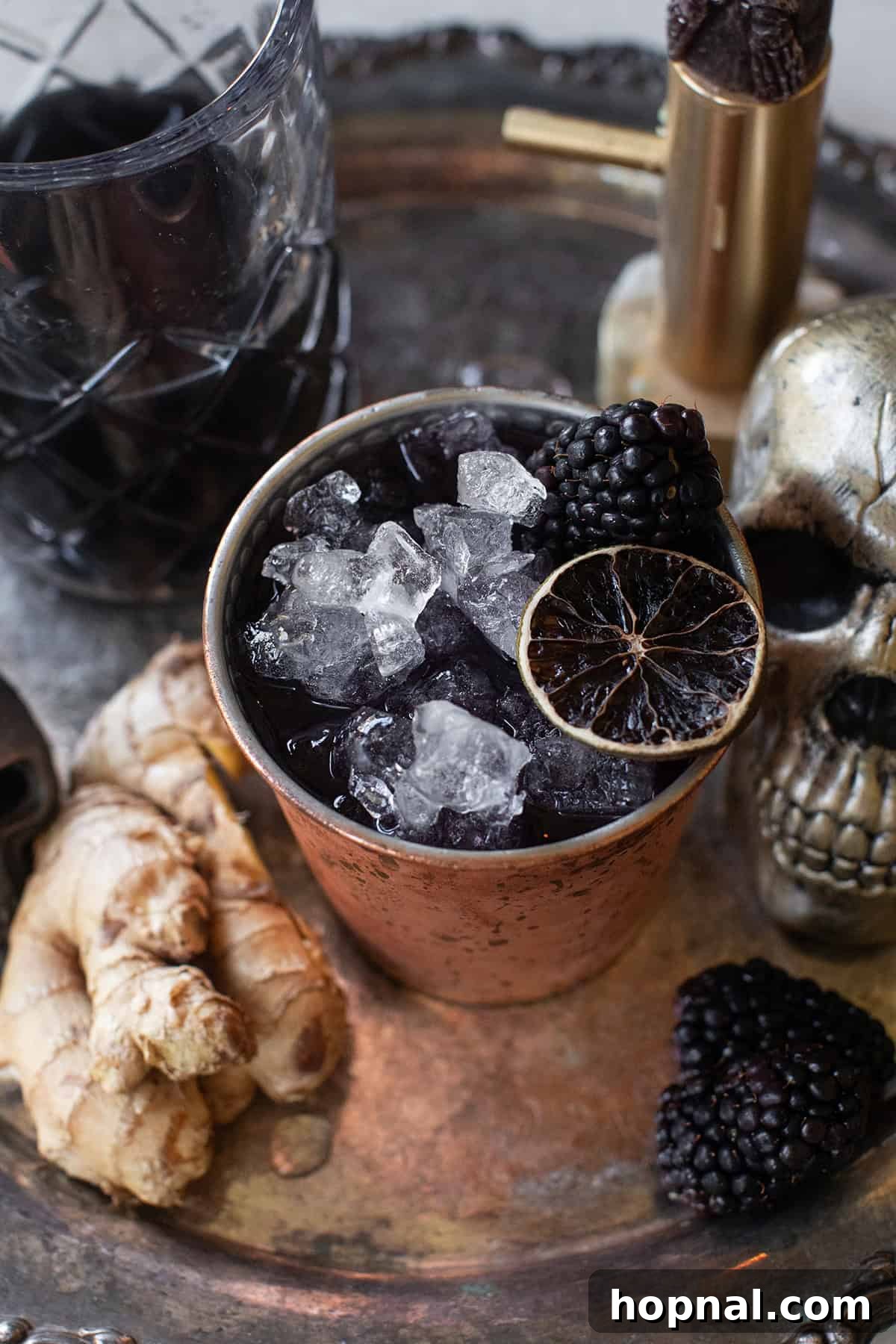 Close-up of a Halloween cocktail made with black vodka, garnished with lime and blackberries.