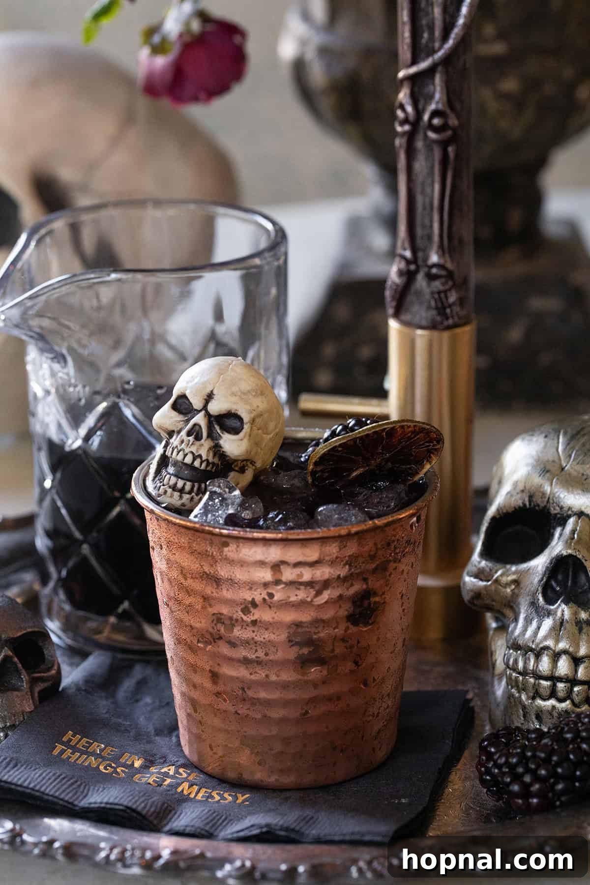 A Halloween cocktail recipe served in a traditional copper mug with skeleton hand decor, perfect for eerie celebrations.