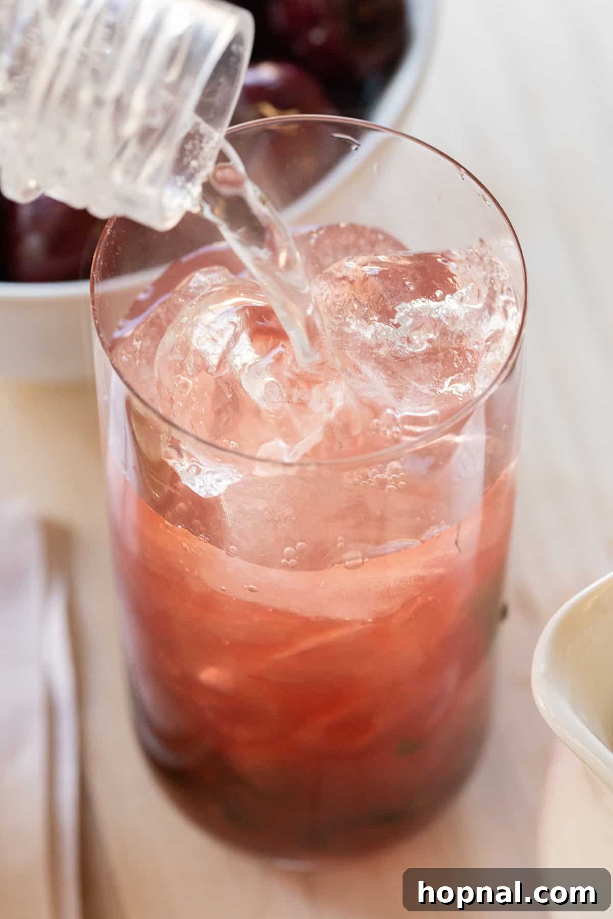 Pouring soda water into cherry juice to make a cherry mojito, demonstrating the fizz and layering of ingredients.