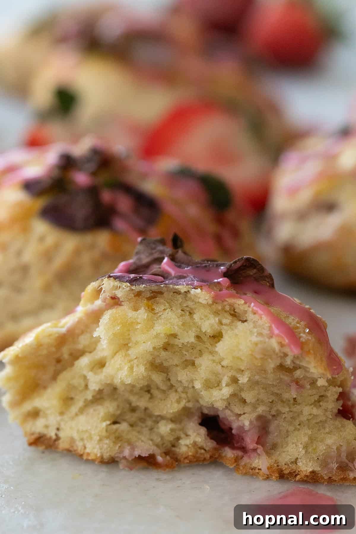 A perfectly baked strawberry scone, gently pulled apart to reveal its tender, flaky interior studded with bright red strawberry pieces.