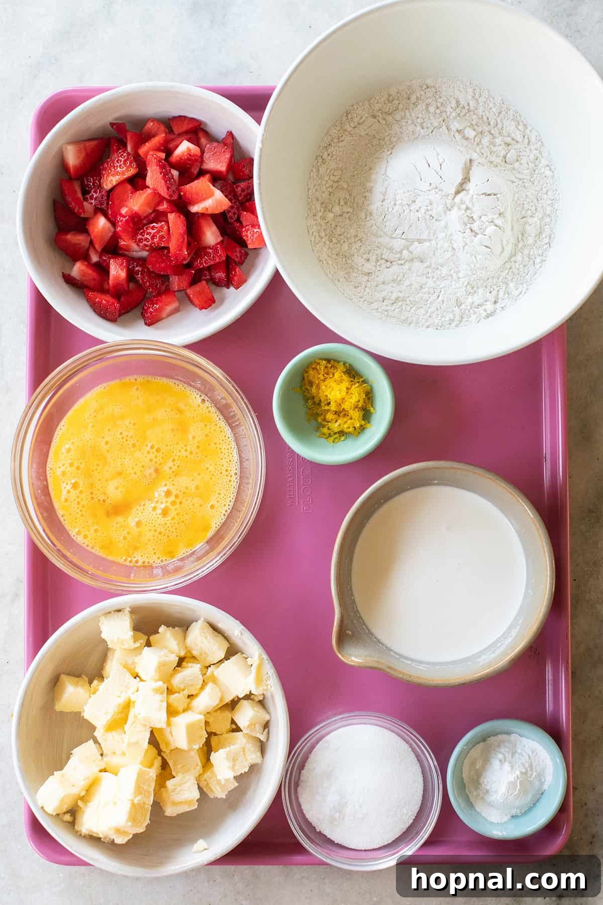 A selection of fresh ingredients laid out on a wooden tray, including cold butter cubes, vibrant fresh strawberries, flour, eggs, and buttermilk, all essential for making perfect strawberry scones.