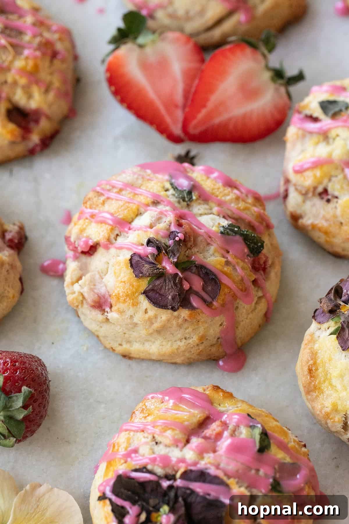 A batch of freshly baked strawberry scones, glistening with a generous drizzle of blood orange glaze, arranged on a cooling rack.