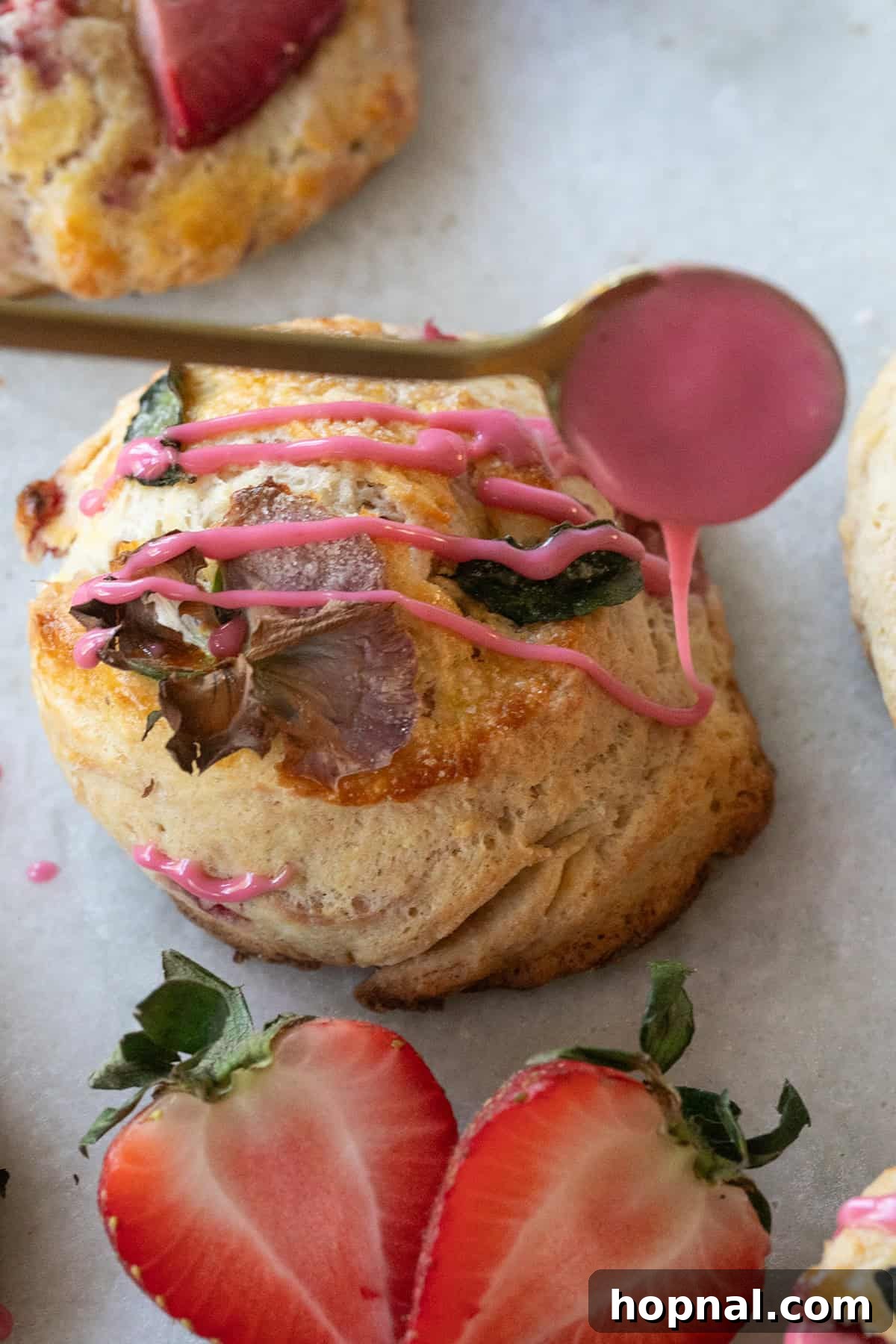 A close-up shot of a hand drizzling vibrant blood orange glaze generously over the golden-brown top of a freshly baked strawberry scone, creating a beautiful pink cascade.