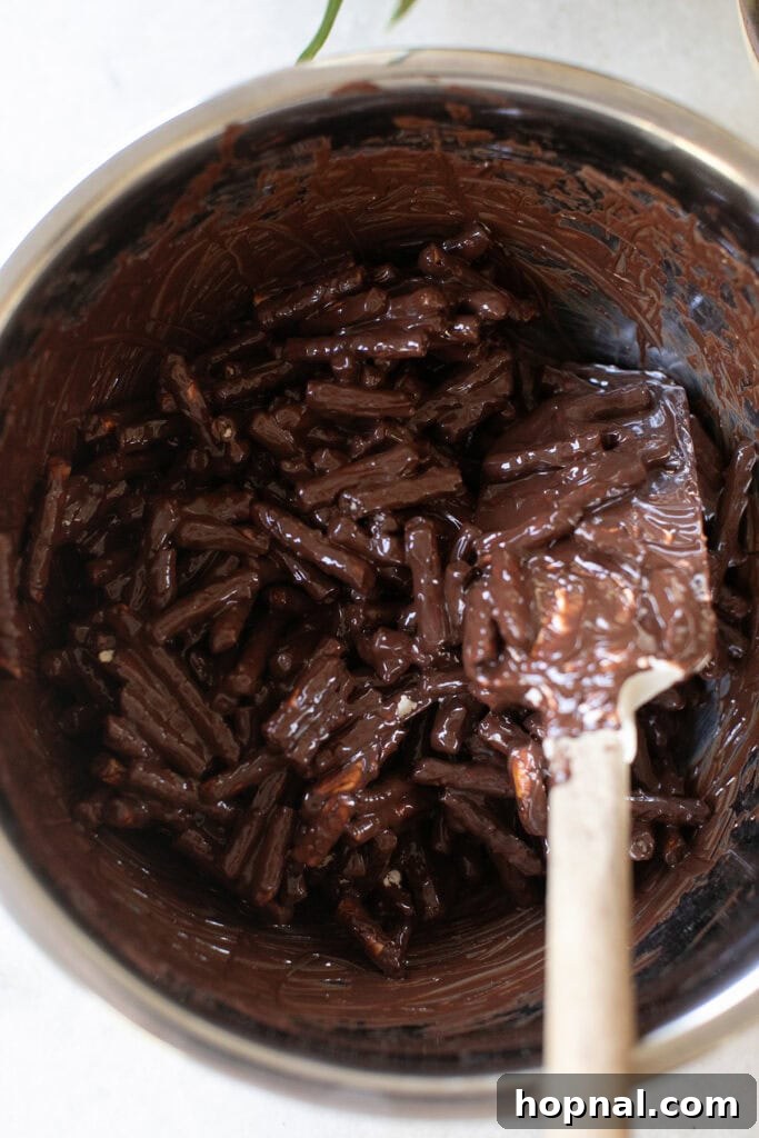Sweet Spring Nests 7 Broken pretzels being gently folded into the melted chocolate and peanut butter mixture in a large bowl, ensuring even coating.