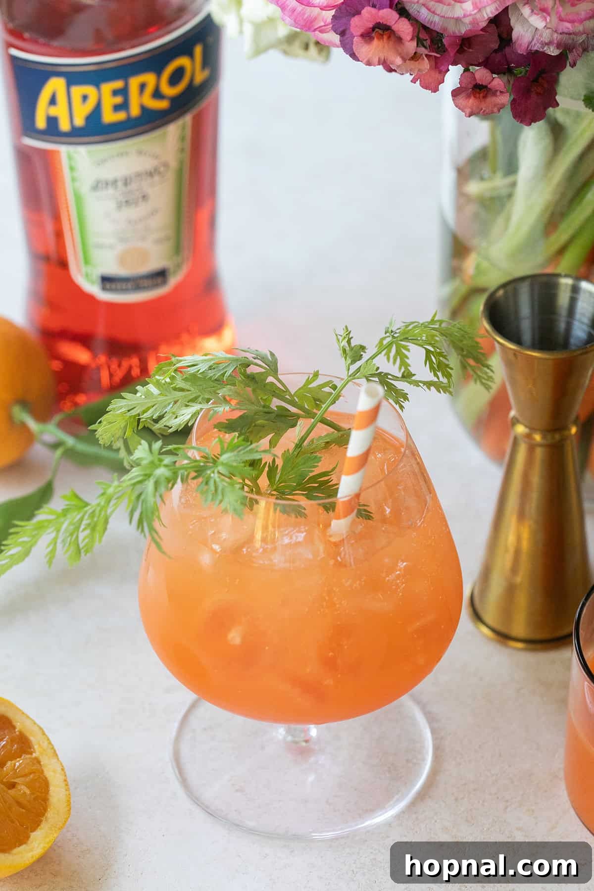 A vibrant Carrot Spritz cocktail in a tall glass, garnished with an orange slice and a delicate, curled carrot ribbon, embodying the freshness of spring.