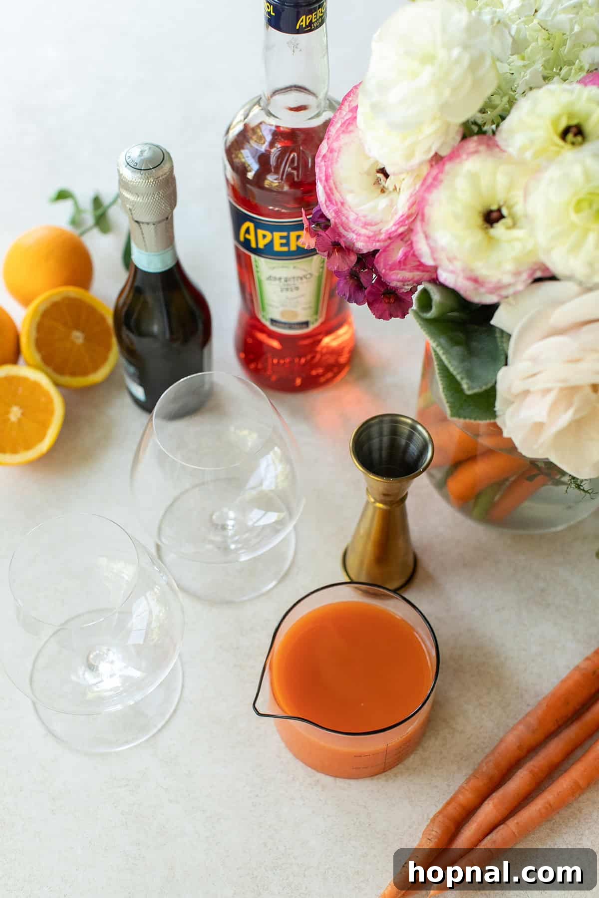 Key ingredients for a Carrot Spritz laid out on a wooden table: fresh carrot juice, vibrant Aperol, bubbly Prosecco, and a glass of orange juice. Ready for mixing.