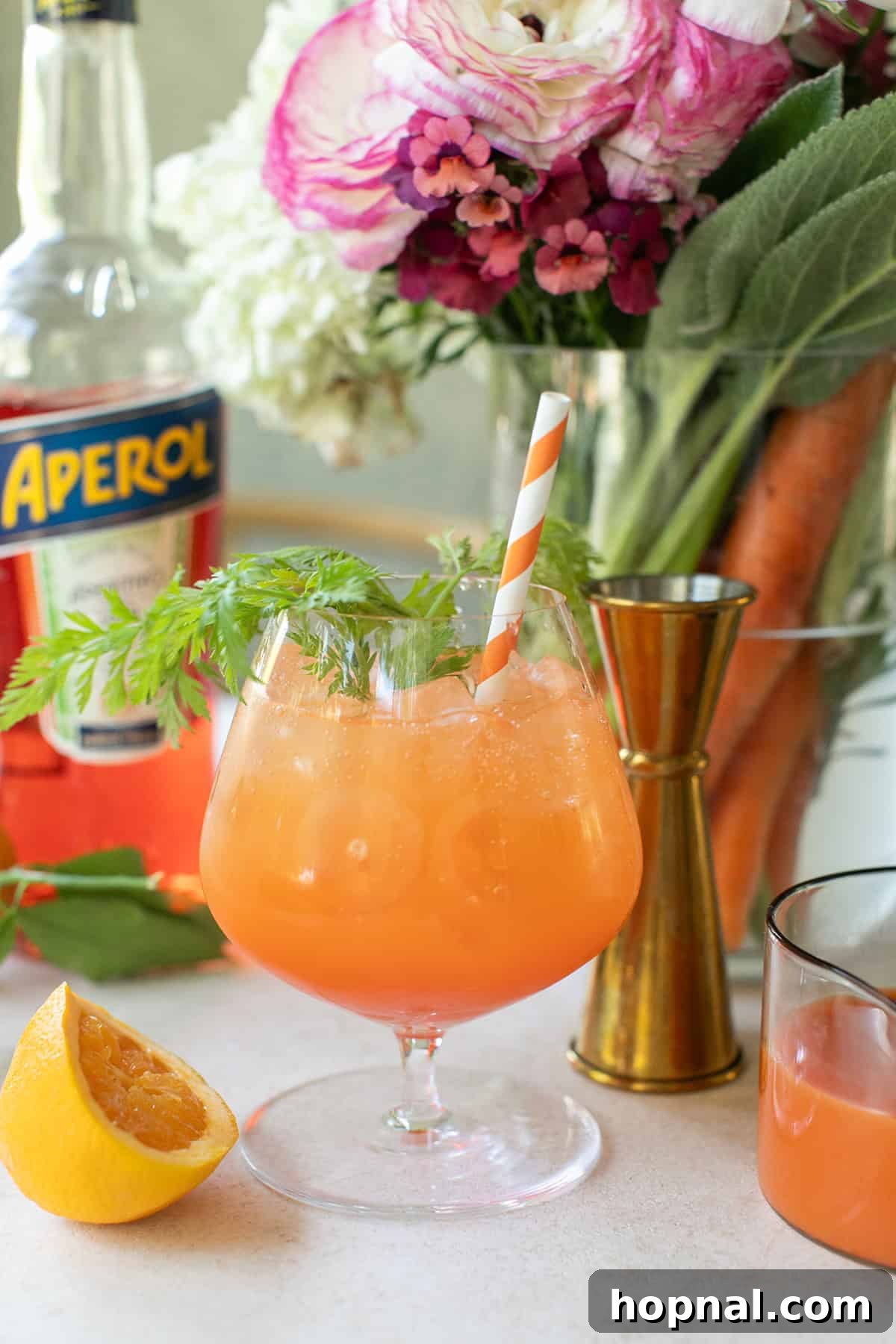 An inviting Carrot Spritz served in a tall glass with an orange straw, garnished with fresh carrot greens, ready for an Easter celebration or sunny afternoon.