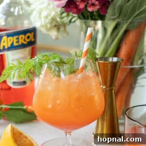 An inviting Carrot Spritz served in a tall glass with an orange straw, garnished with fresh carrot greens.